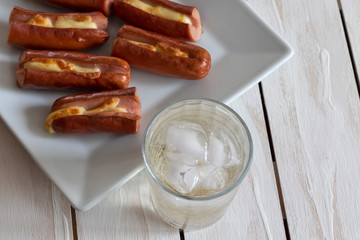 Roasted sausage with yellow cheese and a glass of soda over white wooden background