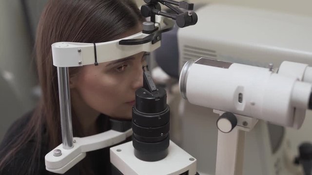 A young beautiful female brunette patience holding her head still in keratometer while female doctor/eyespecialist/ophthalmologist examining the patience. Medical concept