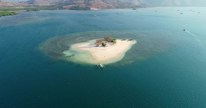 Aerial, drone shot towards a paraw boat and a man, on a small, Gili Kedis, sand island, on the coast of Lombok, on a sunny day, in Indonesia