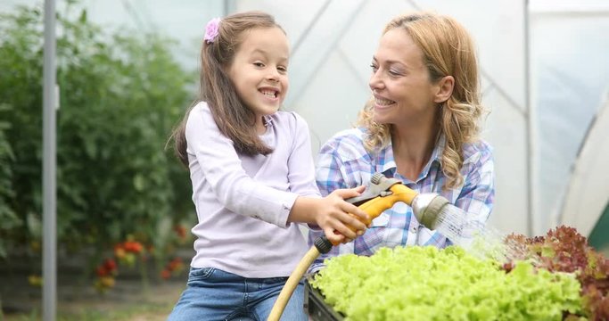 Farming, gardening, agriculture and people concept. Happy mother and her daughter working at greenhouse
