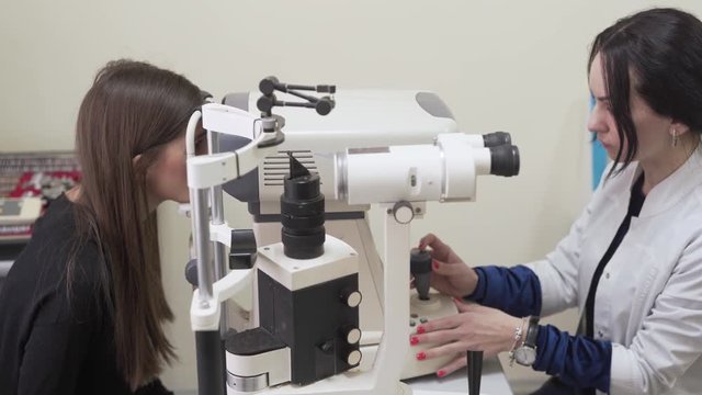 A young beautiful female brunette sitting ophthalmologist office. Female doctor examining patience with keratometer. Medical concept