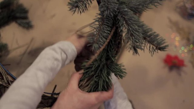 Close up of child and adult hands winding up christmas tree branches with a wire to make a wreath. Kids masterclass of weaving wreath for Christmas
