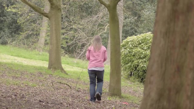 Woman walks through woodland trees