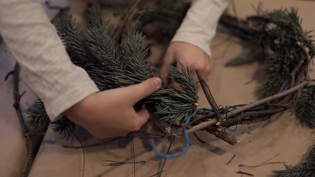 Close up of child hands winding up christmas tree branches with a wire to make a wreath. Kids masterclass of weaving wreath for Christmas