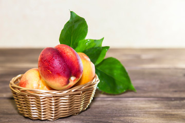Food, harvest, fresh fruit. Ripe fruit of juicy peach with water drops and leaves in a wicker basket on a wooden background in a rustic style with a copy space