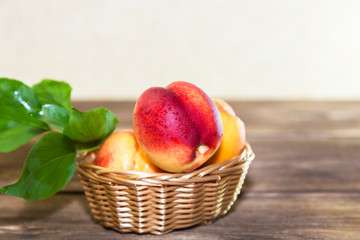 Food, harvest, fresh fruit. Ripe fruit of juicy peach with water drops and leaves in a wicker basket on a wooden background in a rustic style with a copy space