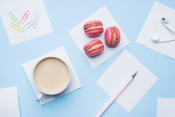 Concept morning Breakfast. Cup of coffee, macaroon cookies and notepad on blue pastel background. Flat lay style.