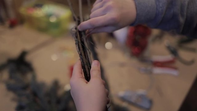 Close up of child hands tightening up wooden rods with a a thin wire making christmas wreath. Pine branch base for christmas wreath. Masterclass of weaving wreath for Christmas