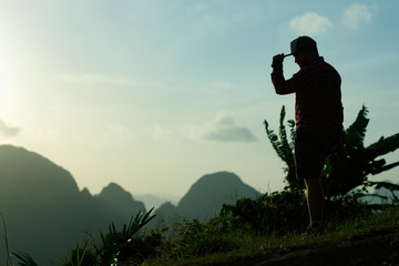 A young photographer with a beard and a cap meets the dawn on a high mountain.