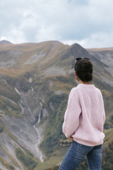Naklejka premium young girl in a sweater is looking at the Caucasian mountains, Georgia, rear view.