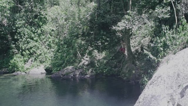 SLOW MOTION: boy swings on a rope swing hanging from a tree and fall into the base of Mango Waterfall in Adjuntas, Puerto Rico.