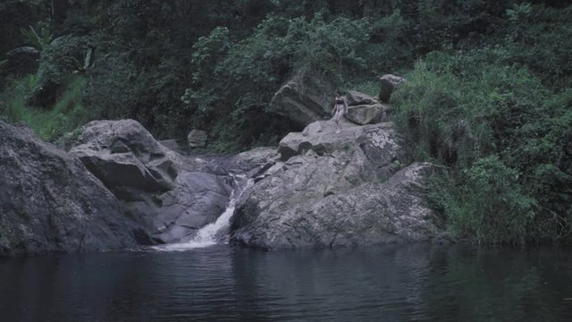 SLOW MOTION: looking over the base of Mango Waterfall in Adjuntas, Puerto Rico as a girl climbs down the rocky structure.