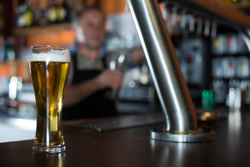 glass of beer on bar counter against background of friendly bartender