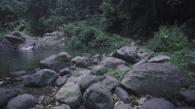 SLOW MOTION: lifting from behind a rocky terrain to reveal a girl, in the distance, entering the base of Mango Waterfall in Adjuntas, Puerto Rico.