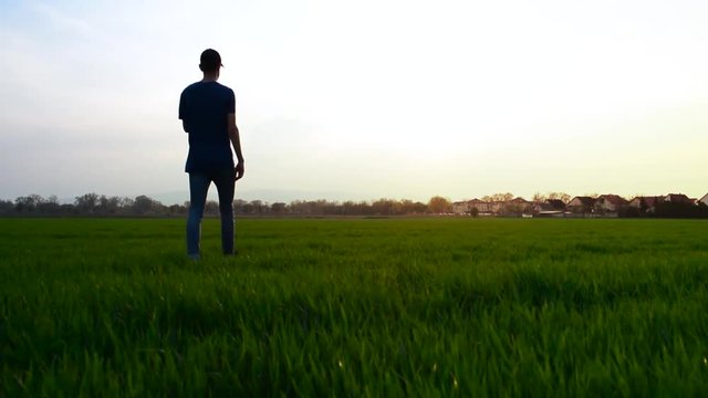 Lonely boy walking towards setting sun while the golden beams of the sun light up the scene.