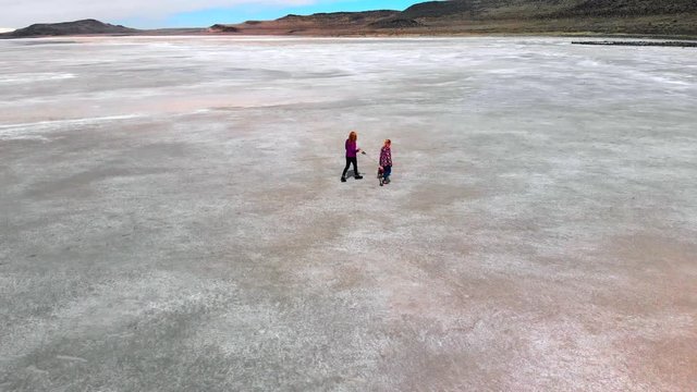 Aerial low level rotating pan of a Mother, daughter and dog walking on a desolate landscape by the great salt lake.