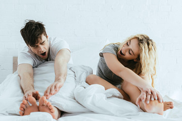 attractive blonde woman and handsome man yawning in bed