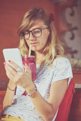 Beautiful woman using cellphone while drinking smoothie outdoors.