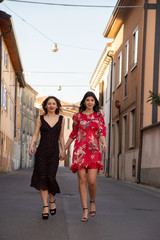 Obraz na płótnie Canvas Full-length portrait of two friends, a blonde in a black dress and the other brunette in a red dress. Breathe a full sense and enjoy freedom. They walk in the middle of the street holding hands. Conce