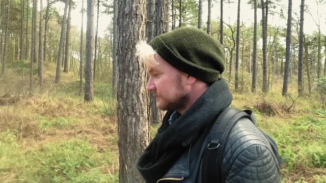 Extreme slow motion shot of authentic caucasian hipster man travelling and hiking through a forest of tall trees on a sunny day.