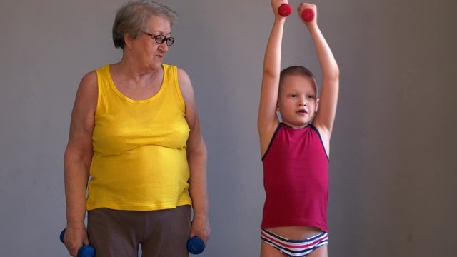 Elderly woman grandmother in yellow shirt doing gymnastics with dumbbells with grandchild