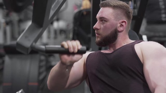Confident bodybuilder training on a chest press with a single arm, close up shot