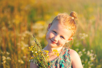 Happy young girl with a flowers and toy in his hand against the green grass