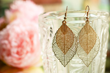 Golden ladies earrings leaves close up on blurred colorful background with flowers.