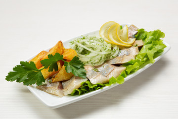 herring lined with slices in a plate with fried potatoes and raw onions, decorated with greens and lemon