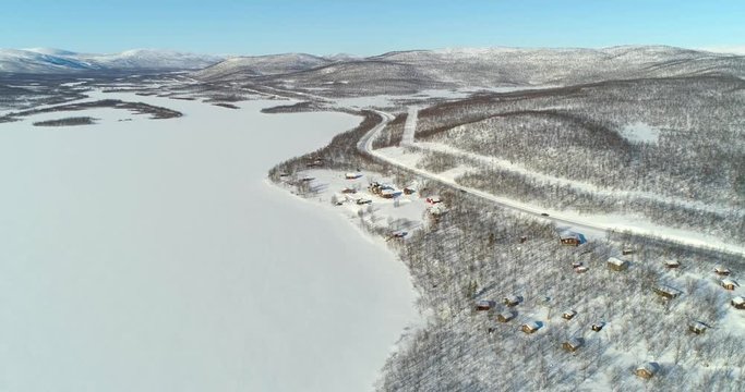 Aerial, static, drone shot, of cars, driving on road e8, between frozen polar lake and boreal wilderness, in Kasivarren eramaa, Enontekio, Lapland, Finland