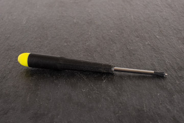 One whole square screwdriver with a yellow black plastic handle work item on grey stone
