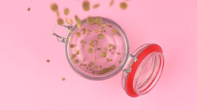 Slow motion image of lentils falling on jar glass over pastel background.