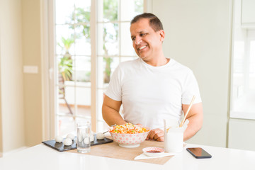 Middle age man eating asian food with chopsticks at home looking away to side with smile on face, natural expression. Laughing confident.