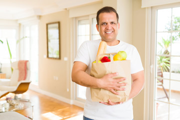 Middle age man holding grocieries bag full of vegetables at home