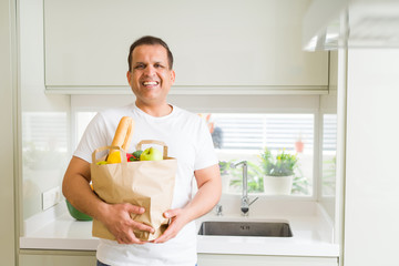 Middle age man holding grocieries bag full of vegetables at home