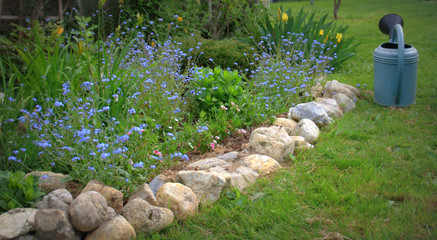 jardin printanier avec fleurs de saison et arrosoir © Patryssia