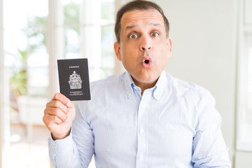 Middle age man holding holding Canadian passport scared in shock with a surprise face, afraid and excited with fear expression