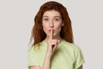 Red-haired girl keep finger on lips asking silence