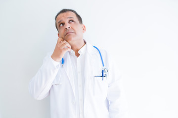 Middle age doctor man wearing stethoscope and medical coat over white background with hand on chin thinking about question, pensive expression. Smiling with thoughtful face. Doubt concept.