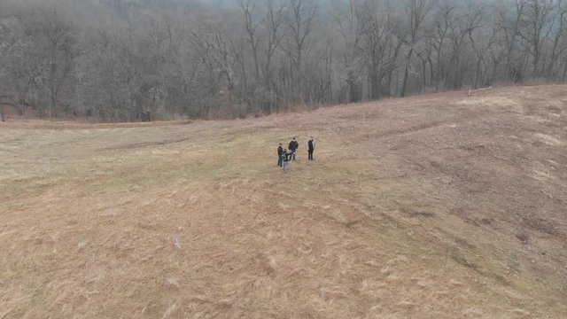 aerial footage spinning in circle of people on a dry pastureland, trees around