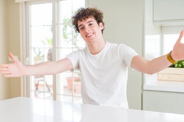 Young handsome man wearing white t-shirt at home looking at the camera smiling with open arms for hug. Cheerful expression embracing happiness.