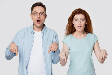 Shocked couple isolated on studio background point down