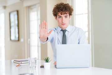 Fototapeta premium Young business man working with computer laptop at the office doing stop sing with palm of the hand. Warning expression with negative and serious gesture on the face.