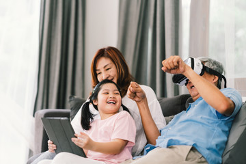 Lovely happy people playing Virtual Reality game together, young kid girl using digital tablet, grandfather wearing VR headset. Family life love relationship, or home fun leisure activity concept