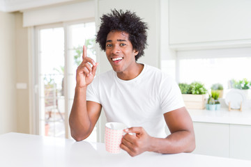 African American man with afro hair drinking a cup of coffee surprised with an idea or question pointing finger with happy face, number one