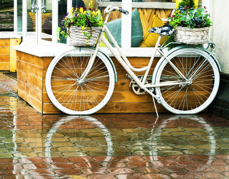 White vintage bicycle with floral baskets standing outside at cafe background. Retro style transport with beautiful flowers