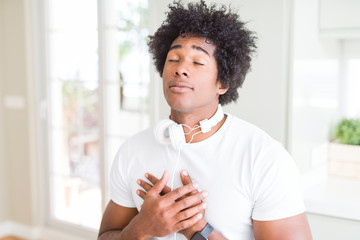 African American man wearing headphones listening to music smiling with hands on chest with closed eyes and grateful gesture on face. Health concept.