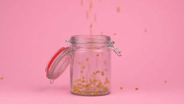 Slow motion image of popcorn falling on jar glass over pastel background.