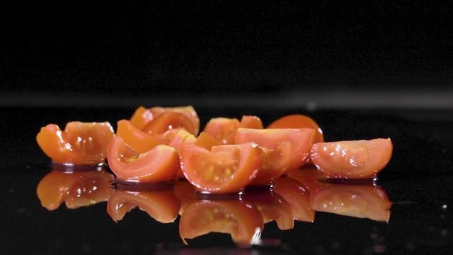 Pomodorini rossi che cadono su un piano bagnato con sfondo nero e schizzano acqua ovunque. Ripresa al rallentatore.