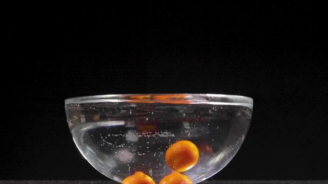 Pomodorini per sugo rosso cadono in una bacinella piena d'acqua facendo schizzi. Sfondo nero, video al rallentatore.